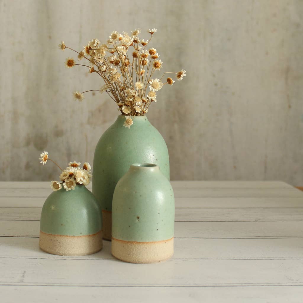 Three mint green ceramic vases with dried flowers on a wooden surface.