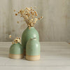 Three mint green ceramic vases with dried flowers on a wooden surface.