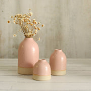 Set of three pink ceramic vases with beige bases on a wooden surface.